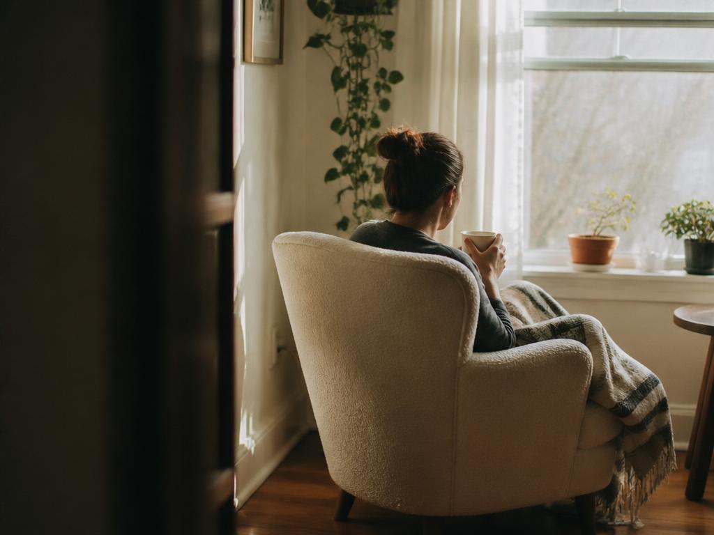 A person seated alone in an armchair by a sunlit window